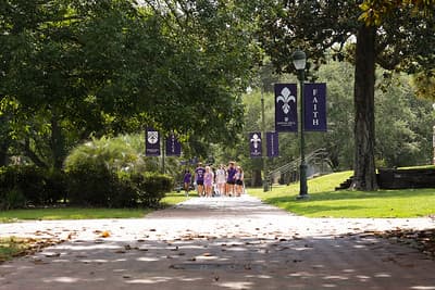 Students walking a tree-lined campus path beneath purple Spring Hill banners